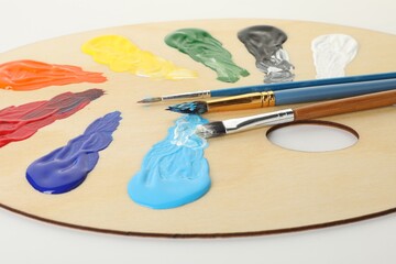 Wooden palette with paints and brushes on white background, closeup