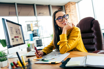 Young businesswoman in a modern office setting, wearing a stylish outfit, smiling while working and...
