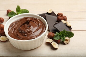 Chocolate hazelnut spread in bowl, nuts, pieces of chocolate and mint on wooden table, closeup