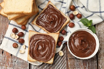 Toasts with chocolate hazelnut spread, nuts and mint on wooden table, flat lay