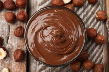 Chocolate hazelnut spread in bowl and nuts on wooden table, flat lay