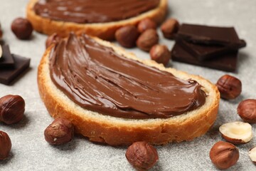 Toasts with tasty chocolate hazelnut spread and nuts on grey table, closeup
