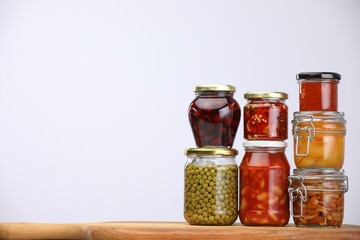 Many jars with different pickled products on wooden board against light grey background, space for text