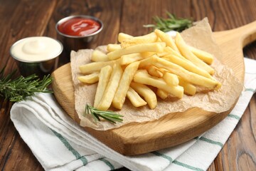 Tasty french fries served with sauces and rosemary on wooden table, closeup