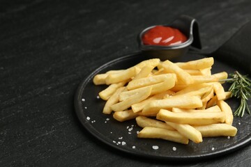 Tasty french fries served with ketchup and rosemary on black table, closeup. Space for text