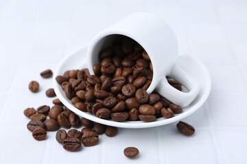 Aromatic coffee beans, cup and saucer on white table, closeup