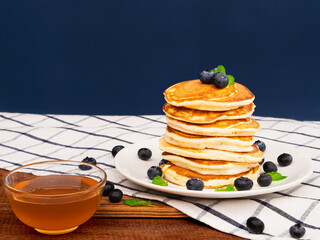 Delicious pancakes with blueberry in white plate and maple syrup on wooden table background....