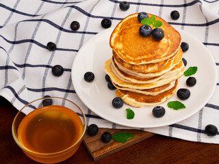 Delicious pancakes with blueberry in white plate and maple syrup on wooden table background. Breakfast