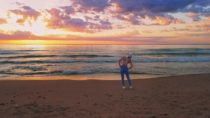 Athletic woman gazing at sunrise, reflecting tranquil wellness amid sandy beach landscape during morning fitness session.Sport outdoors concept, filmed by drone