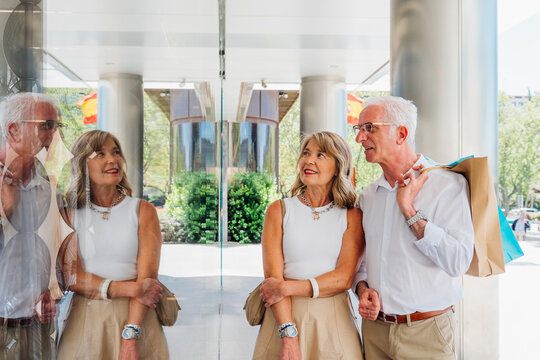 An older couple window shopping, carrying shopping bags, strolling through the sunny city streets. - Powered by Adobe