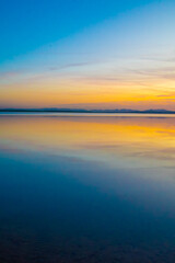 Naklejka premium Sunset over a still lake with golden and blue tones reflecting in calm water. A peaceful and tranquil natural scene with a soft gradient sky.