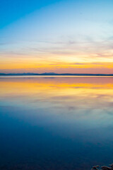Colorful sunset reflecting on a calm lake surface. Vivid tones of purple, yellow, and blue create a magical and serene atmosphere.