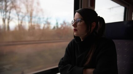 Portrait of beautiful young brunette in glasses at table in train car looking out window. Adventures and change of scenery give new emotions and sense of freedom. Travel and tourism concept