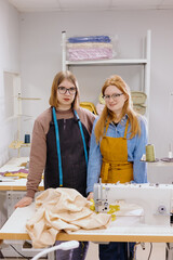 Two female seamstresses in workshop at factory are standing at a table with sewing machines. fashion design, creating a fashion collection for sale. shopping online. women are professional tailors. 