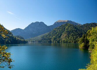 A charming landscape revealed through the branches of trees is the famous Lake Ritsa, located in the mountains of Abkhazia. A warm day in October