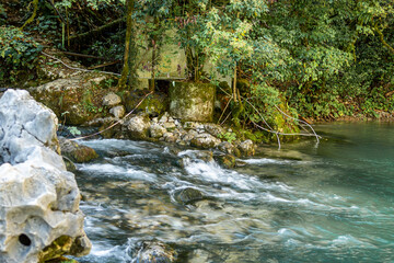 Obraz premium A river rapid of water flowing out of the crystal clear mountain lake Ritsa. The river Yupshara flows out of Lake Ritsa. 