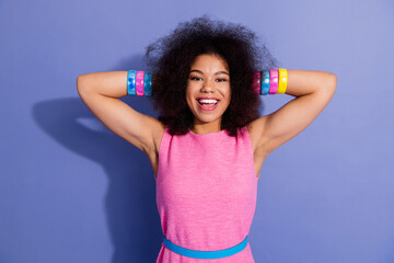 Stylish young woman in pink outfit against purple background expressing joy with hands raised and...