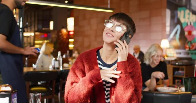 Woman talking by phone at cafe. Woman with short haircut and glasses. Female spending work break at cafe. Woman chatting by phone. Woman during beakfast at cafe. Phone call at cafe.