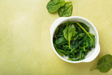 Freshly steamed spinach leaves in a white bowl, resting on a green backdrop, promoting healthy...