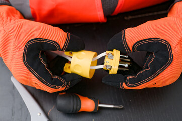 Electrician wearing protective gloves repairing industrial electrical plug