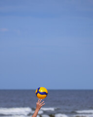 Obraz premium Child's hand throws up bright orange blue ball with a close-up on the sea background