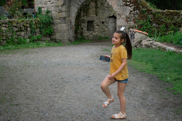 a moment of youthful exploration near ancient ruins. shows a young girl walking with a phone in her hand near weathered stone structures Ideal for themes of childhood adventure history and exploration