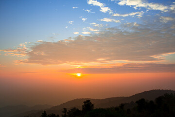 Mountain view at sunrise or sunset, with orange sky in the background and shadows of trees in the foreground from low light in the morning or evening.