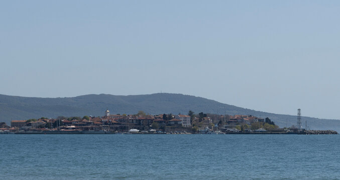 A panoramic view of the ancient town of Nessebar, situated on a peninsula in the Black Sea, featuring its historical architecture, red-tiled roofs, and surrounding blue waters under a clear sky.
