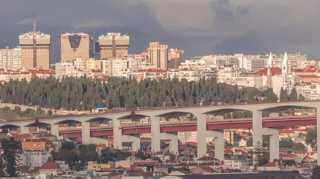 Aerial timelapse of Lisbon skyline featuring colorful houses, Amoreiras shopping center towers and the 25th of April Bridge. Historic district with green trees and Prazeres Cemetery in the foreground