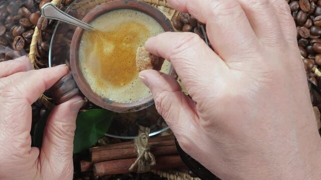 An elderly man puts a piece of sugar into a cup of espresso coffee. View from above. Coffee. Hands, close-up. Slow motion.