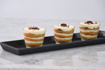 classic Tiramisu Dessert in clear glasses showcasing layers of coffee soaked, and dusted cocoa topped with whipped cream, and chopped nuts side view of Italian dessert