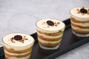 classic Tiramisu Dessert in clear glasses showcasing layers of coffee soaked, creamy mascarpone, and dusted cocoa topped with whipped cream, and chopped nuts closeup view of Italian dessert