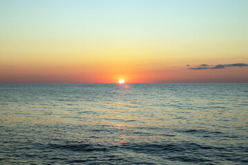 The sun is setting over the ocean, casting a warm glow on the water