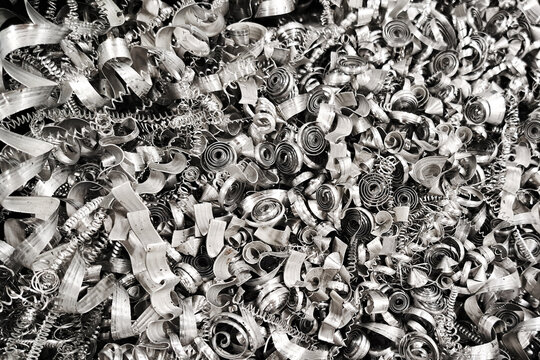 Shiny metal shavings texture. Curled and twisted silver steel spirals. Industrial waste after machining. Bright metallic background with sharp edges. Recycled scrap steel from factory tools.