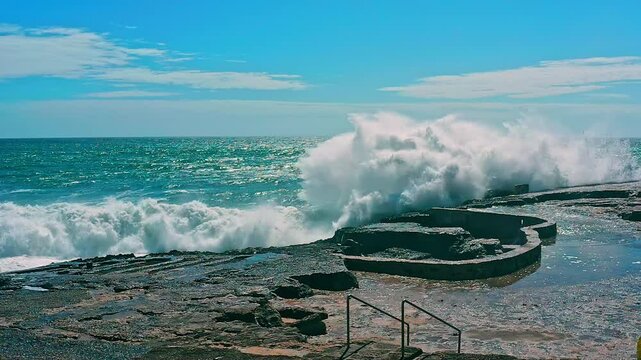 Large ocean waves crash about the  pier - slow motion. Big waves is  crashing on rock creating huge splashes. Beautiful azure ocean waves crashing about cape.  Powerful nature energy. Portugal.
