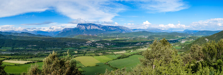 Breathtaking panoramic view of green agricultural valley with dramatic mountain range under blue sky with clouds. Scenic landscape of Spanish Pyrenees from Guaso viewpoint, Huesca province, Aragon