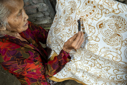 Indonesian artisan drawing traditional batik pattern on fabric
