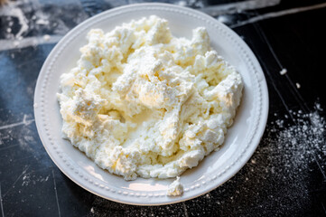 White plate with fresh cottage cheese placed on a stone countertop. A simple and natural dairy product presentation, ideal for healthy eating themes, food packaging, recipes, and nutrition content.