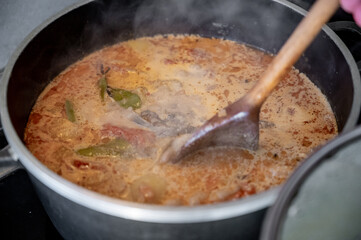 Top-down view of a pot filled with hearty soup, such as bograch or a creamy cheese-based soup. A wooden spoon rests over the pot, filled with steaming broth.