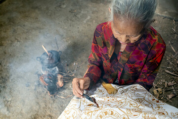 Indonesian woman making traditional batik using canting and hot wax