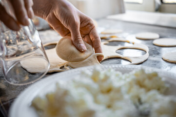 Forming the dough for the varenyky with a glass. Traditional Ukrainian varenyky with cottage cheese - a step-by-step process of home cooking. Hands at work, fresh ingredients and real Eastern European
