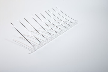 Curved and straight stainless steel spikes aligned on transparent base in continuous row on white...