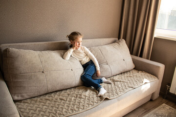 Young girl sitting on cozy sofa wearing casual clothing, with soft textures and warm lighting creating comfortable home atmosphere