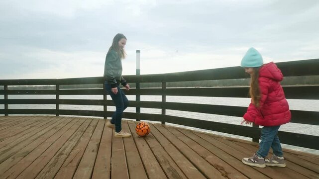 Mother and daughter at the pier near the water having fun. Mom with little girl playing a ball