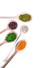Vertical image of various legumes in wooden spoons on white background. Healthy vegetarian and vegan food ingredients, including lentils, beans, and peas. Natural plant protein concept. 