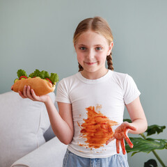 The child stained his clothes with ketchup. A girl eats a hot dog.