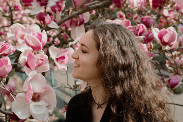 Naklejka premium young woman looking at pink magnolia flowers and smiling