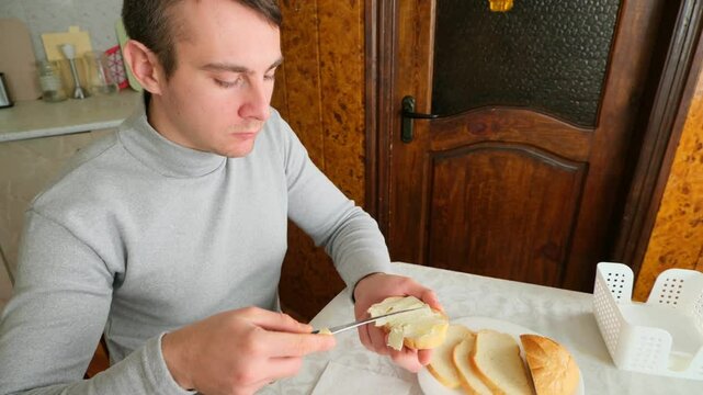Man sitting at the table is buttering a slice of bread in the kitchen