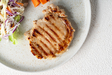 Juicy grilled pork chop steak with fresh vegetables and black pepper sauce on a plate
