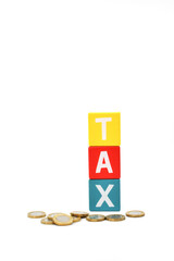 British one pound coins in front of coloured wooden blocks spelling the word Tax isolated against a plain white background